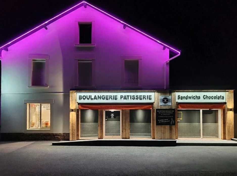 Façade nocturne d'une boulangerie-pâtisserie française, éclairée par des néons violets en bordure de toiture