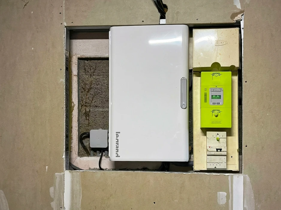 Tableau électrique encastré dans une niche murale en béton, composé d'un coffret Legrand blanc avec poignée centrale, un compteur électrique Linky Enedis vert, et des disjoncteurs modulaires