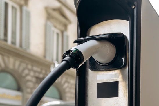 Scène extérieure urbaine avec véhicule électrique en charge sur voie pavée, environnement verdoyant avec arbres en arrière-plan, ambiance résidentielle calme