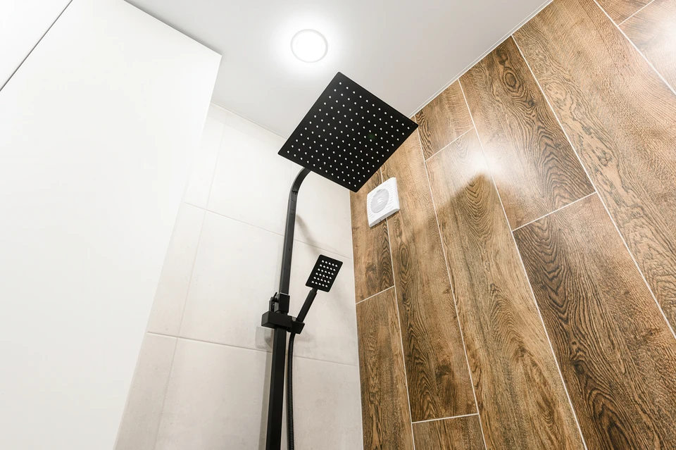 Un carreleur professionnel en polo bleu pose des carreaux de céramique blancs sur un mur de salle de bain